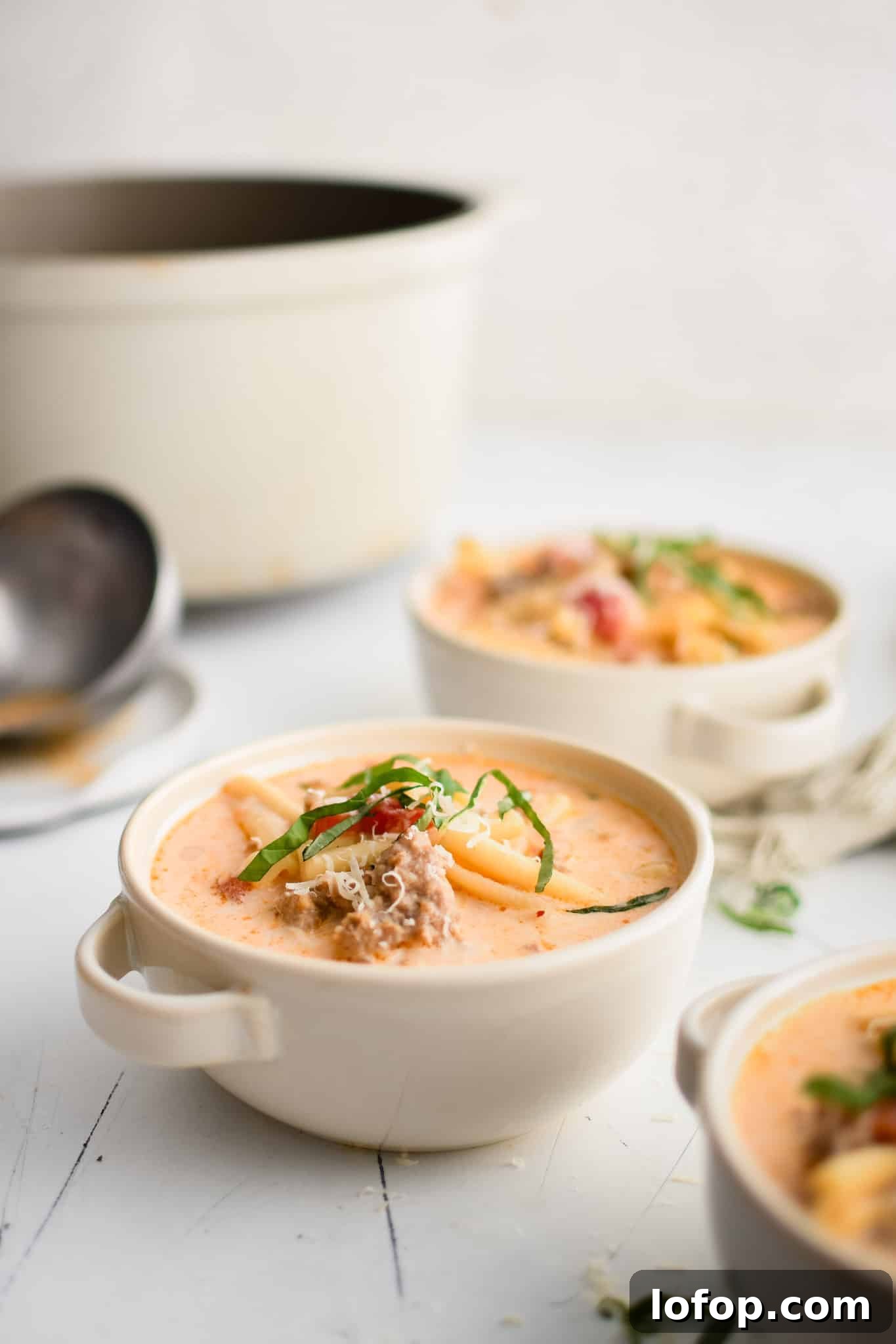 Three soup bowls filled with homemade Italian sausage soup garnished with fresh basil.
