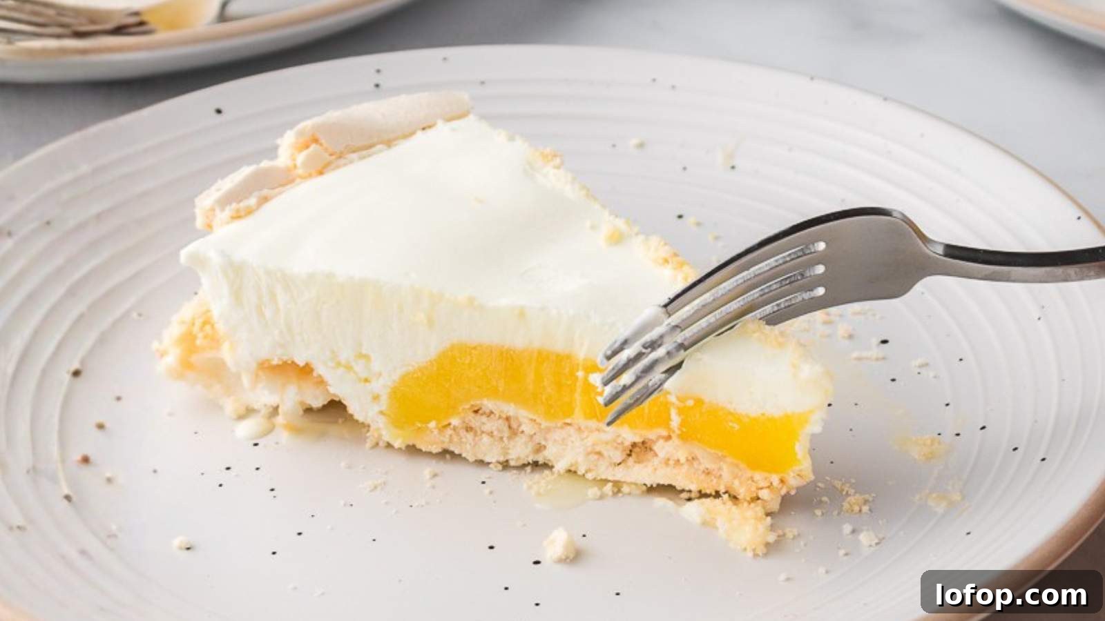 15 Decadent Low-Calorie Desserts That No One Will Suspect Are Light 2 A fork cutting into a slice of angle pie with a white creamy topping and a yellow filling on a white plate.