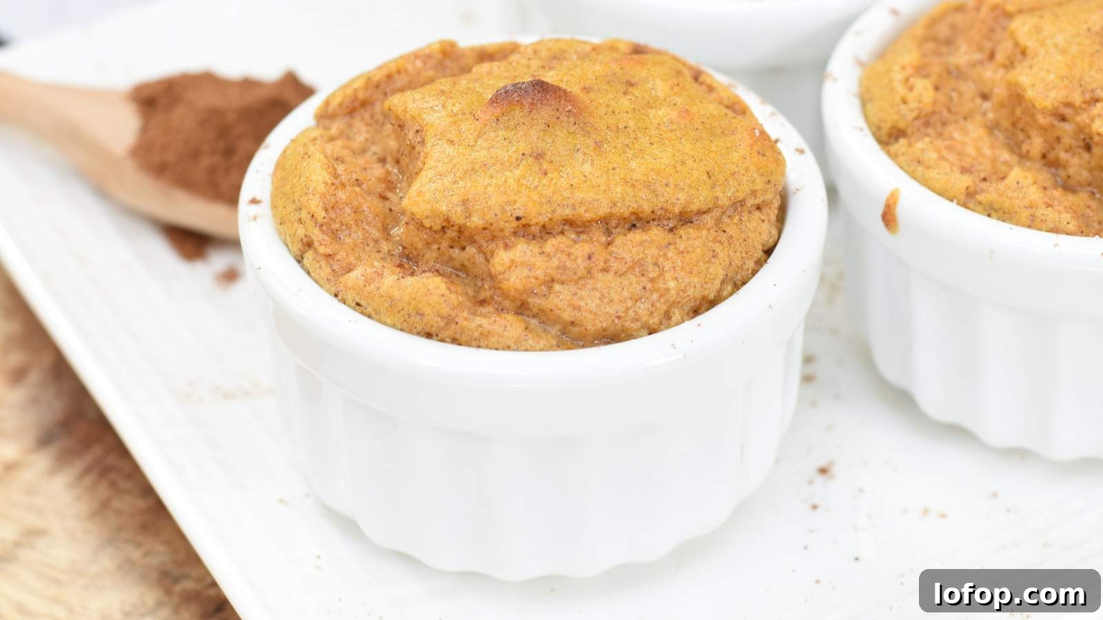 15 Decadent Low-Calorie Desserts That No One Will Suspect Are Light 14 A baked soufflé in a white ramekin sits on a white plate with a wooden spoon and ground cinnamon in the background.