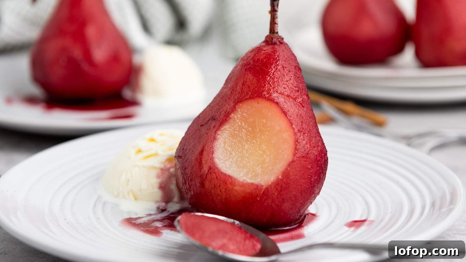 15 Decadent Low-Calorie Desserts That No One Will Suspect Are Light 3 A poached pear with a section scooped, served with a scoop of vanilla ice cream and sauce on a white plate, with a spoon in front.