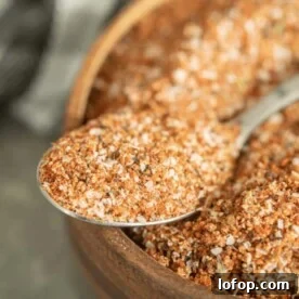 Spoonful of turkey rub resting on the edge of a wooden bowl full of the same rub.